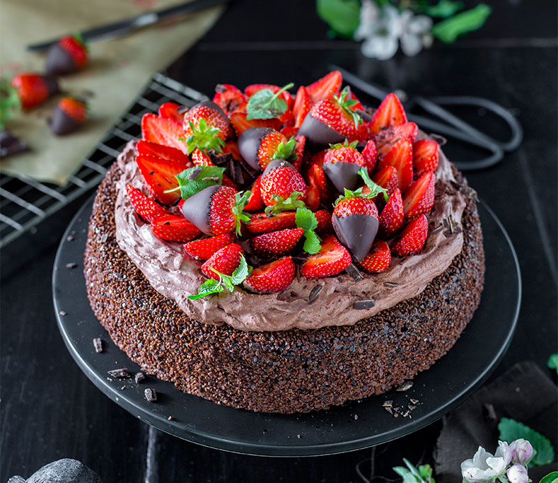 Schokoladentorte mit Erdbeeren verziert auf schwarzem Teller